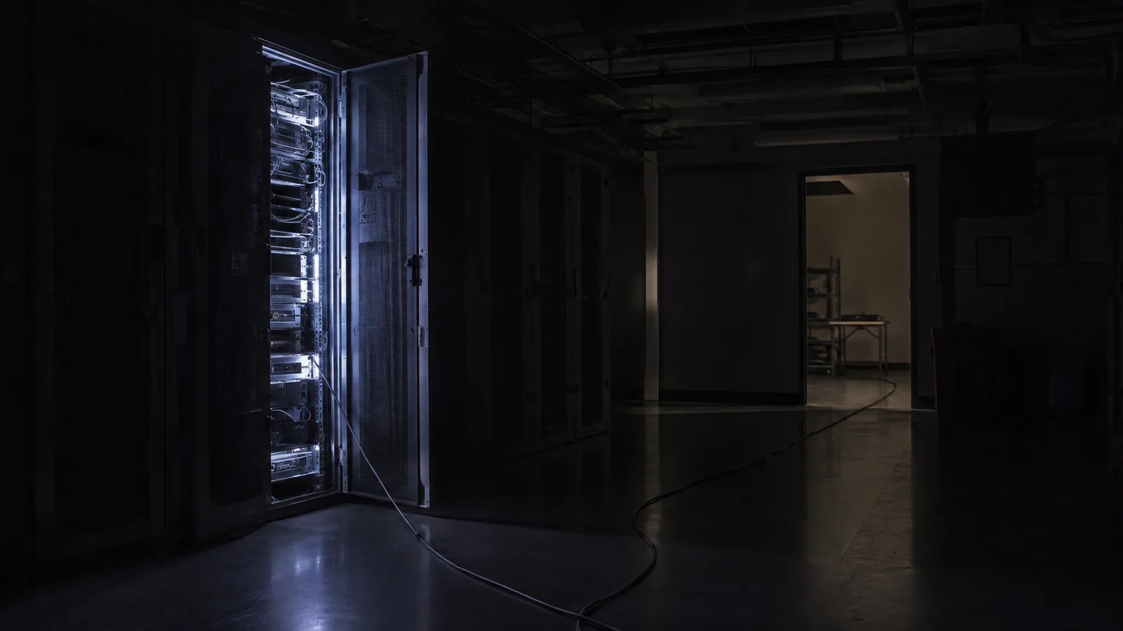 A test lab at night — one rack door ajar, a cable trailing toward the door