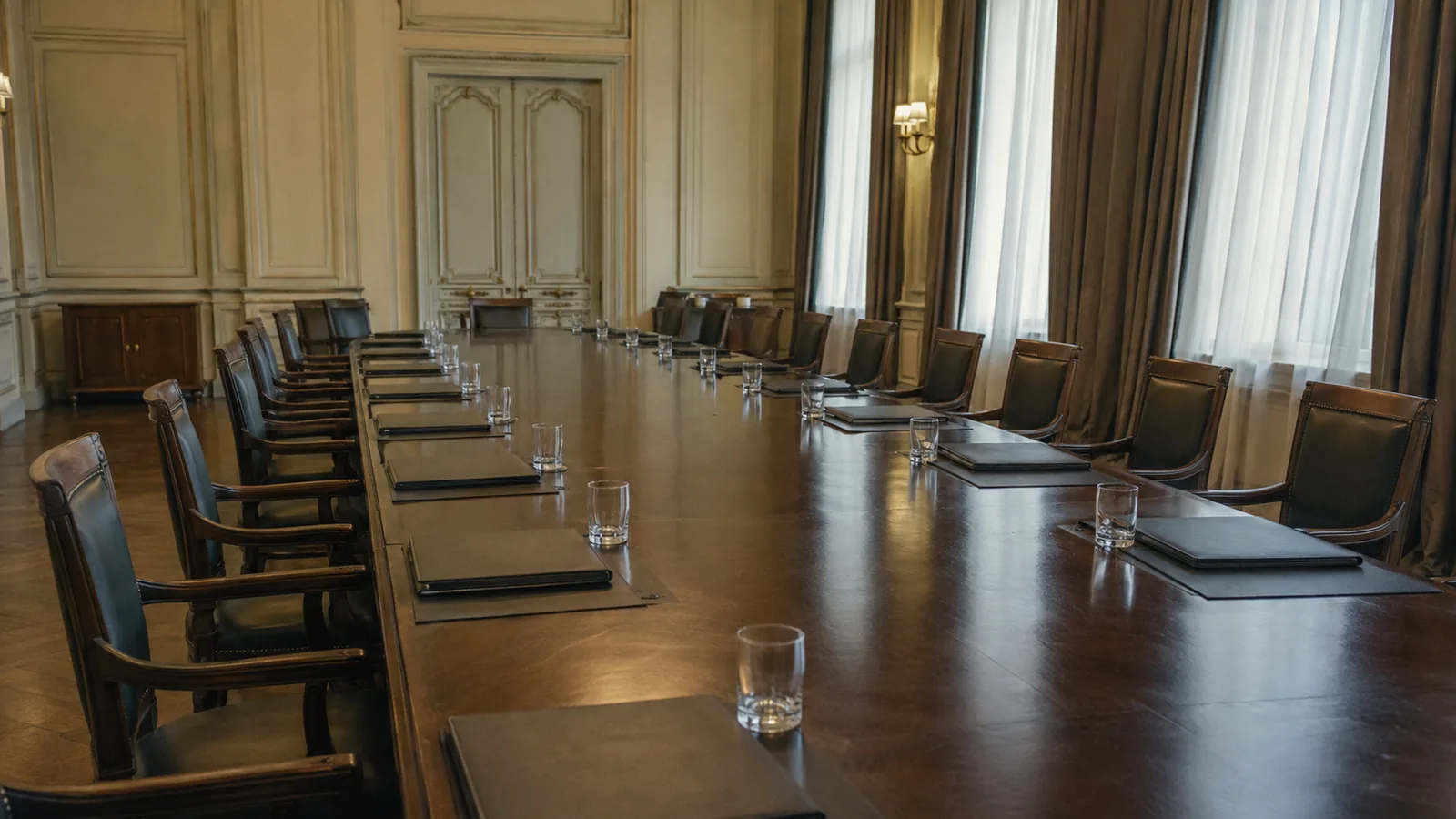 A negotiation hall after talks — closed folders and water glasses left on a long table