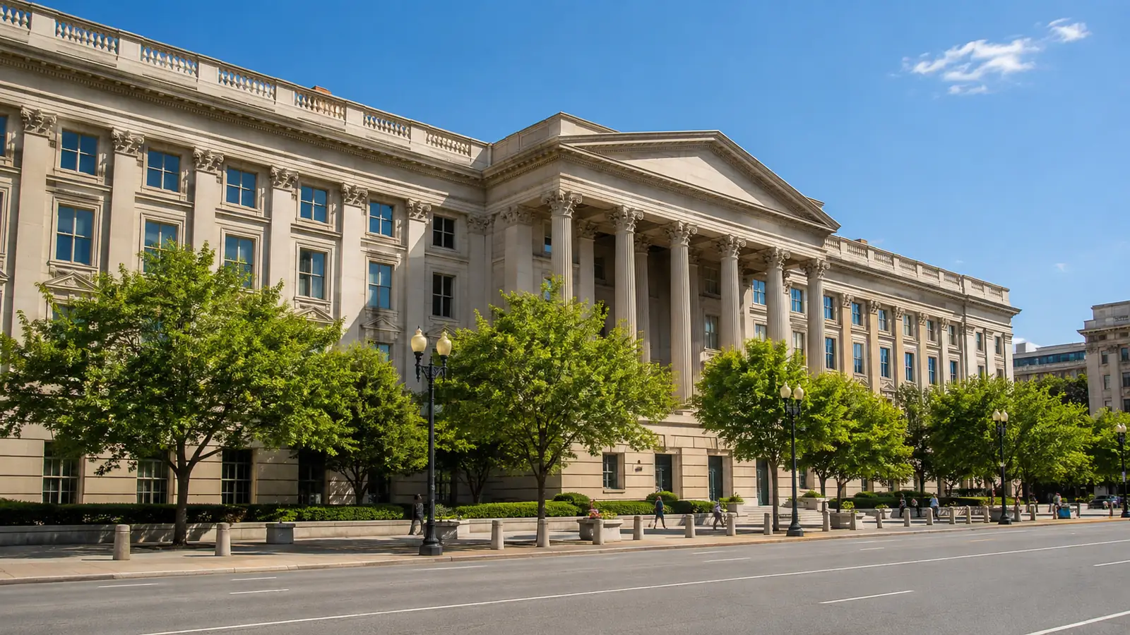 A classical stone government finance building in warm morning light seen from across a tree-lined street