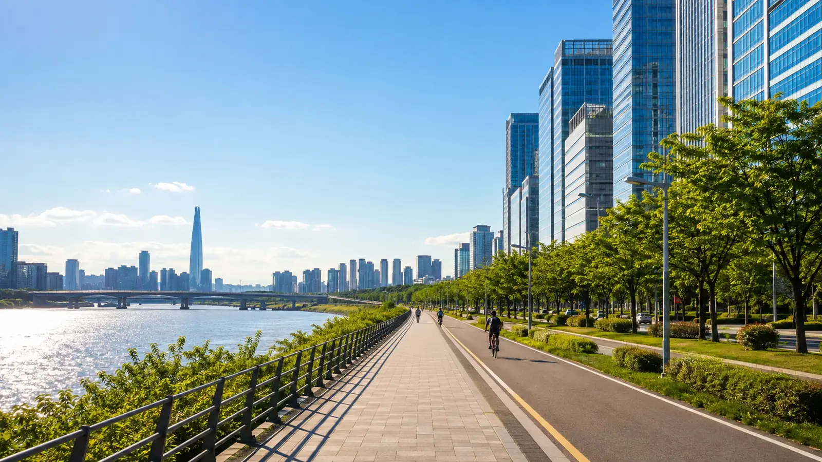 A sunlit riverside boulevard beside glass towers in Seoul, with distant cyclists