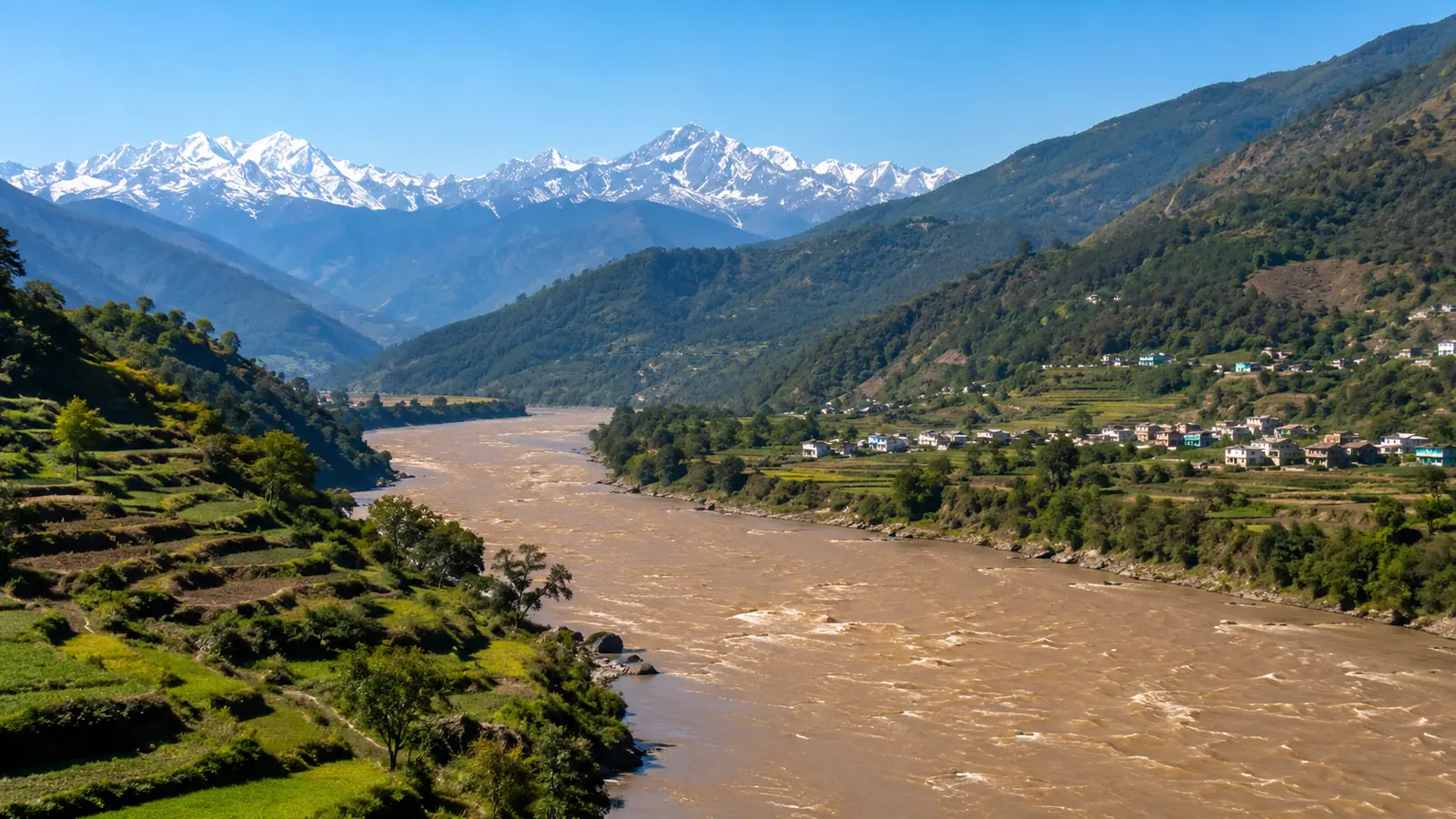 A Himalayan river valley in clear morning light, a swollen brown river winding between green terraced hillsides below distant snow peaks