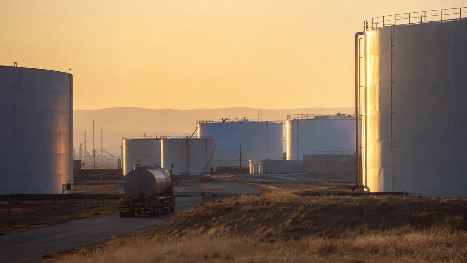 Storage tanks at golden hour as a tanker truck drives away