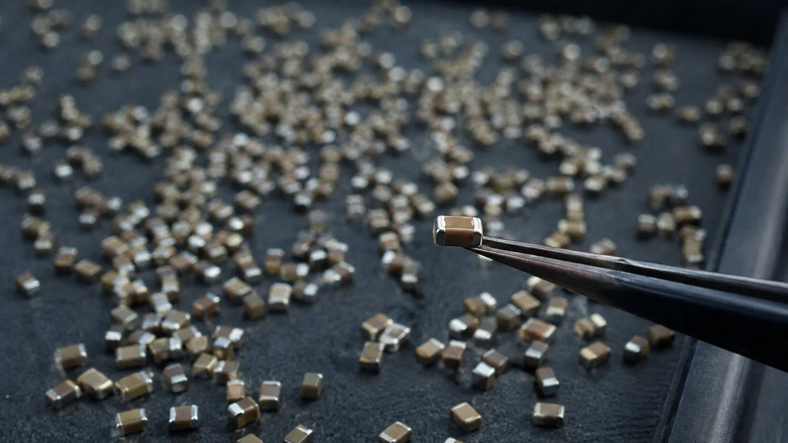 Thousands of tiny ceramic components on a dark tray, one in sharp focus