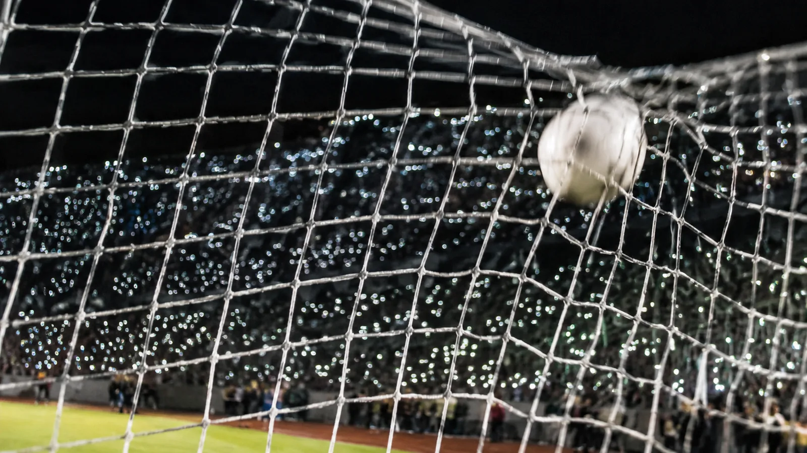 A football resting in the back corner of a goal net at night, the netting still bulging from the impact