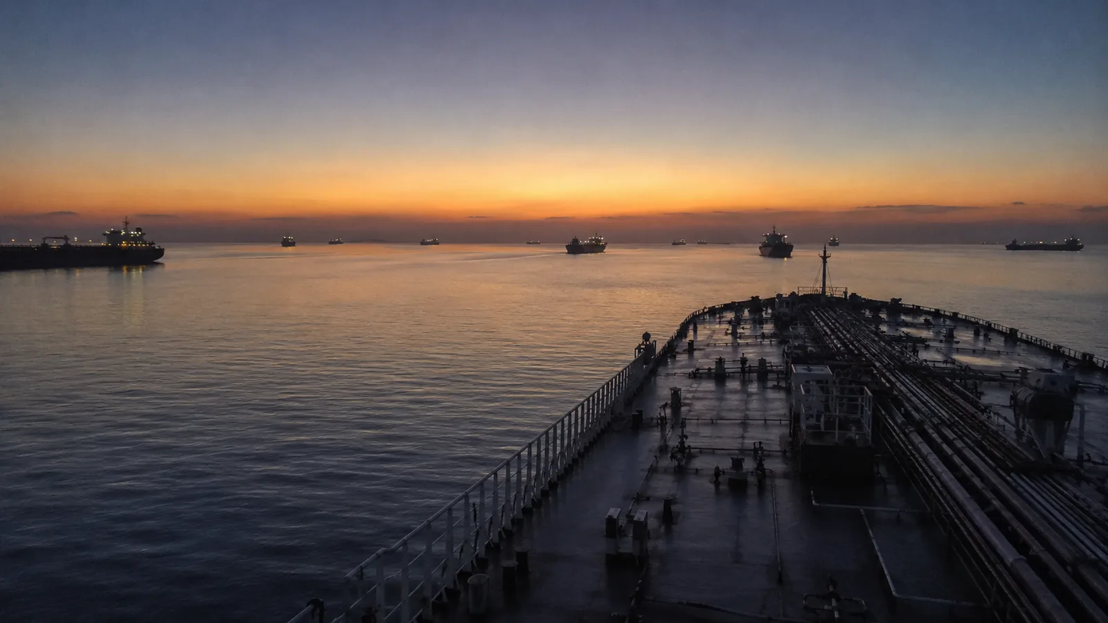 Tankers waiting at anchor in a strait at dawn, an empty shipping lane opening between them