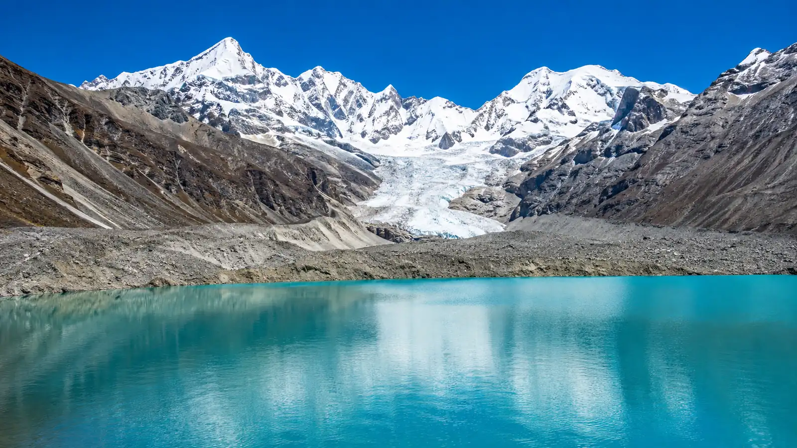 A turquoise glacial lake high in the mountains on a clear day, held back by a long grey ridge of rock and gravel with a glacier tongue behind