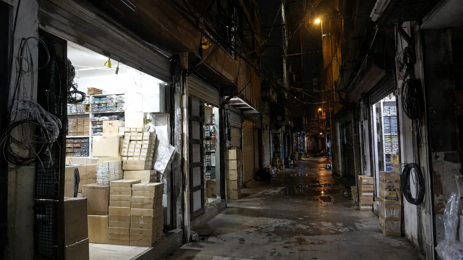 밤의 전자상가 골목 — 상자 더미와 케이블, 반쯤 열린 셔터